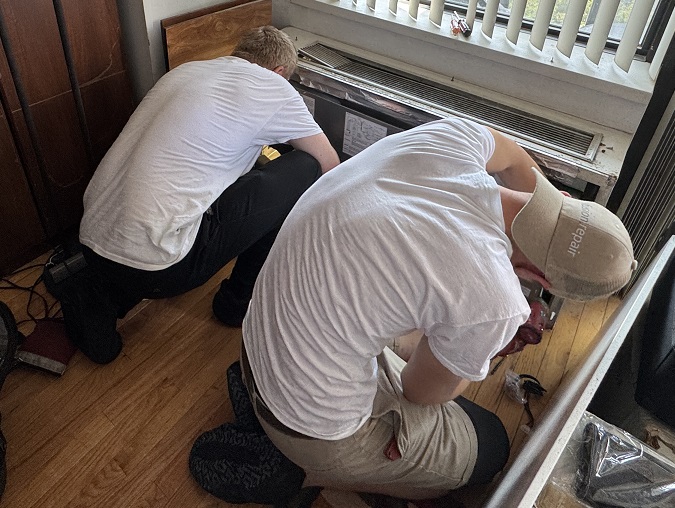 Two HVAC technicians working on a packaged terminal unit